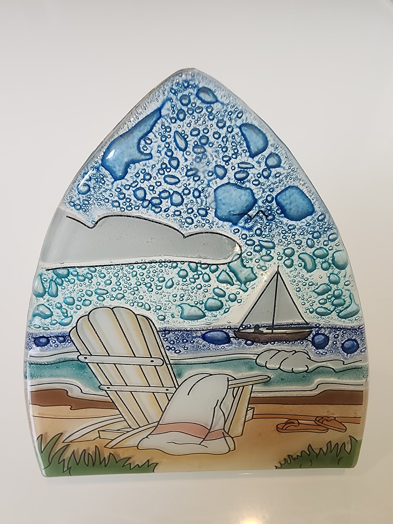 Decorative fused glass night light with abstract blue patterns and a sailboat on the ocean, beach chair on the sand with a towel 
