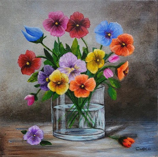 Colorful bouquet of Pansy flowers in a glass vase on a wooden surface with a gray background.